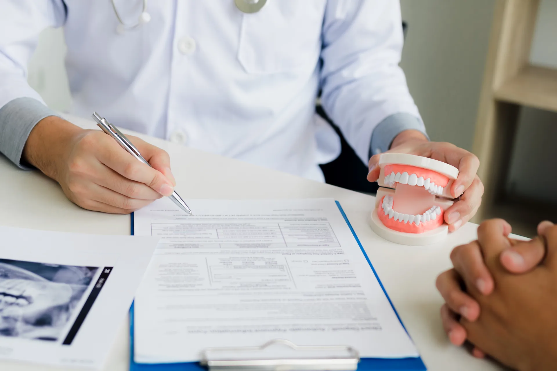 Dentist explaining treatment plan to a patient using a dental model and X-ray