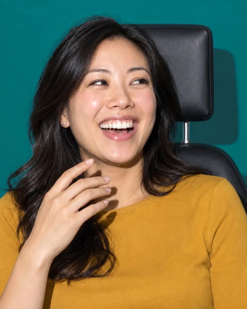 A woman laughs in a dental chair as her hand drops from her mouth.