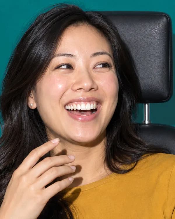 A woman laughs in a dental chair as her hand drops from her mouth.